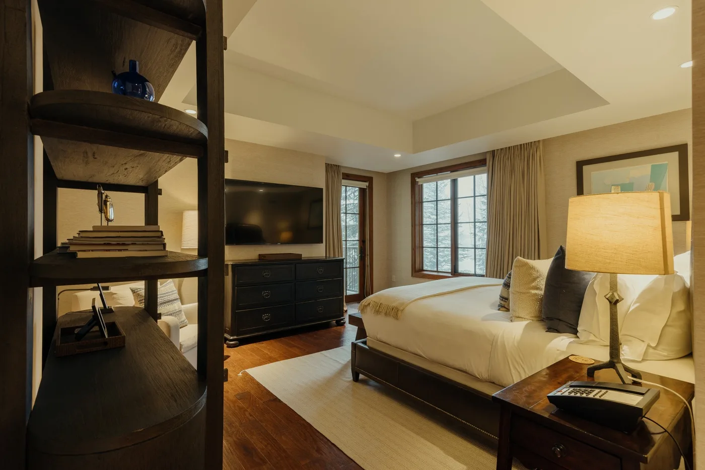 A bedroom with a bed, bedside lamp, and television beside the windows.