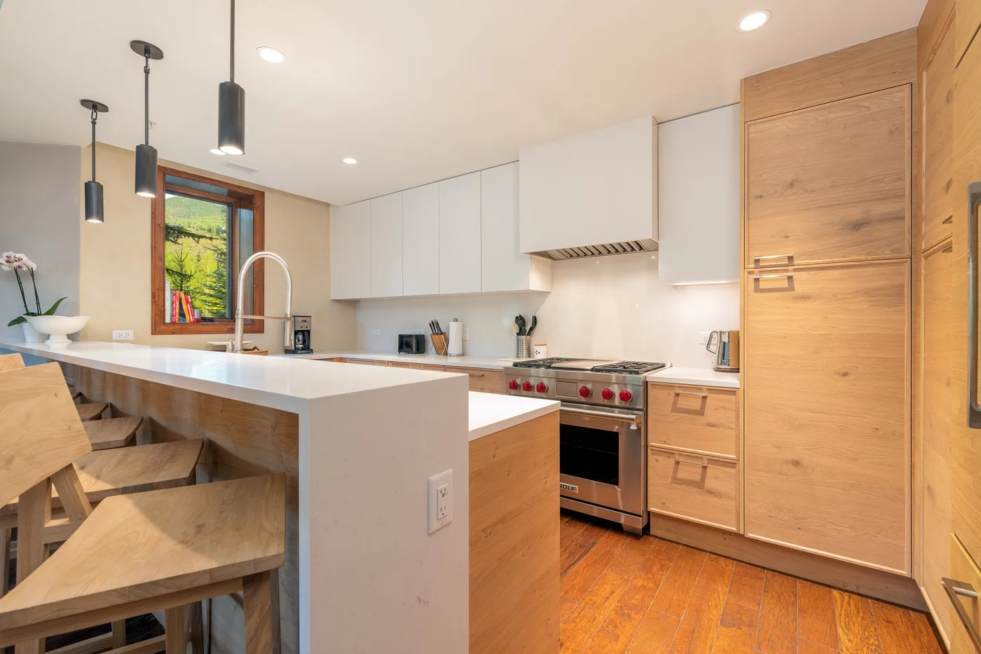 A bright modern kitchen with a central island, wooden cabinetry, and stainless steel appliances.