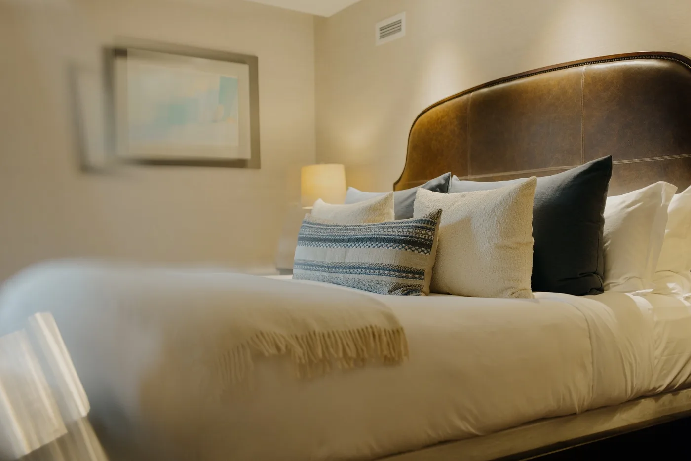 A neatly made bed with layered pillows and a framed picture on the wall.