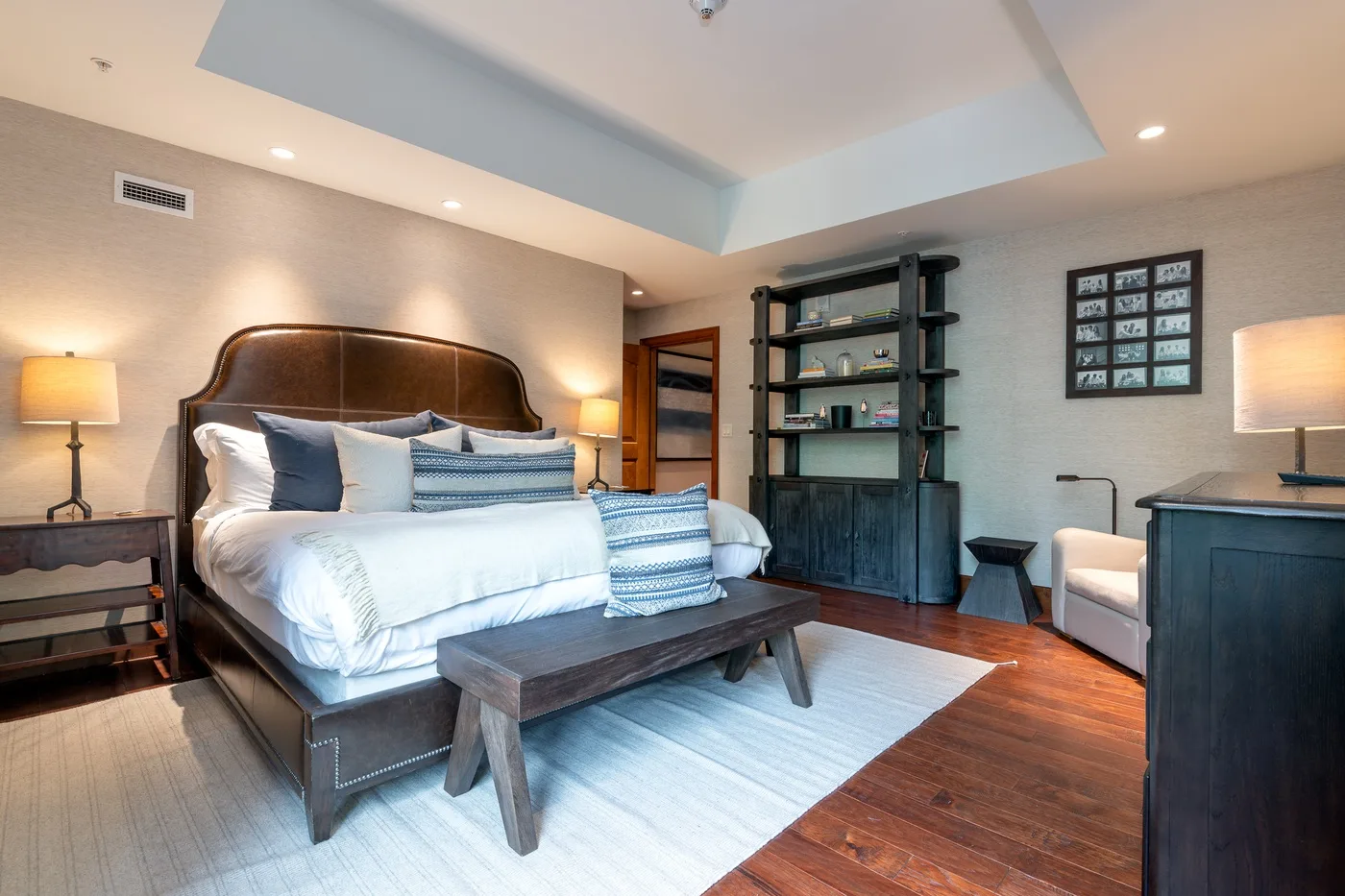 A bedroom with a large bed, bedside lamps, and a dark wooden shelving unit.