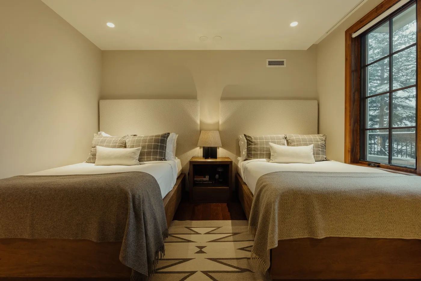 A bedroom with two beds, neutral bedding, and a large window.