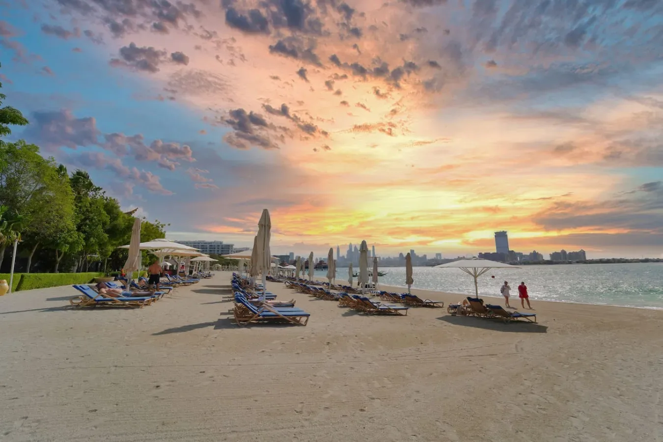 Una playa de arena con tumbonas y sombrillas bajo un cielo colorido al atardecer.