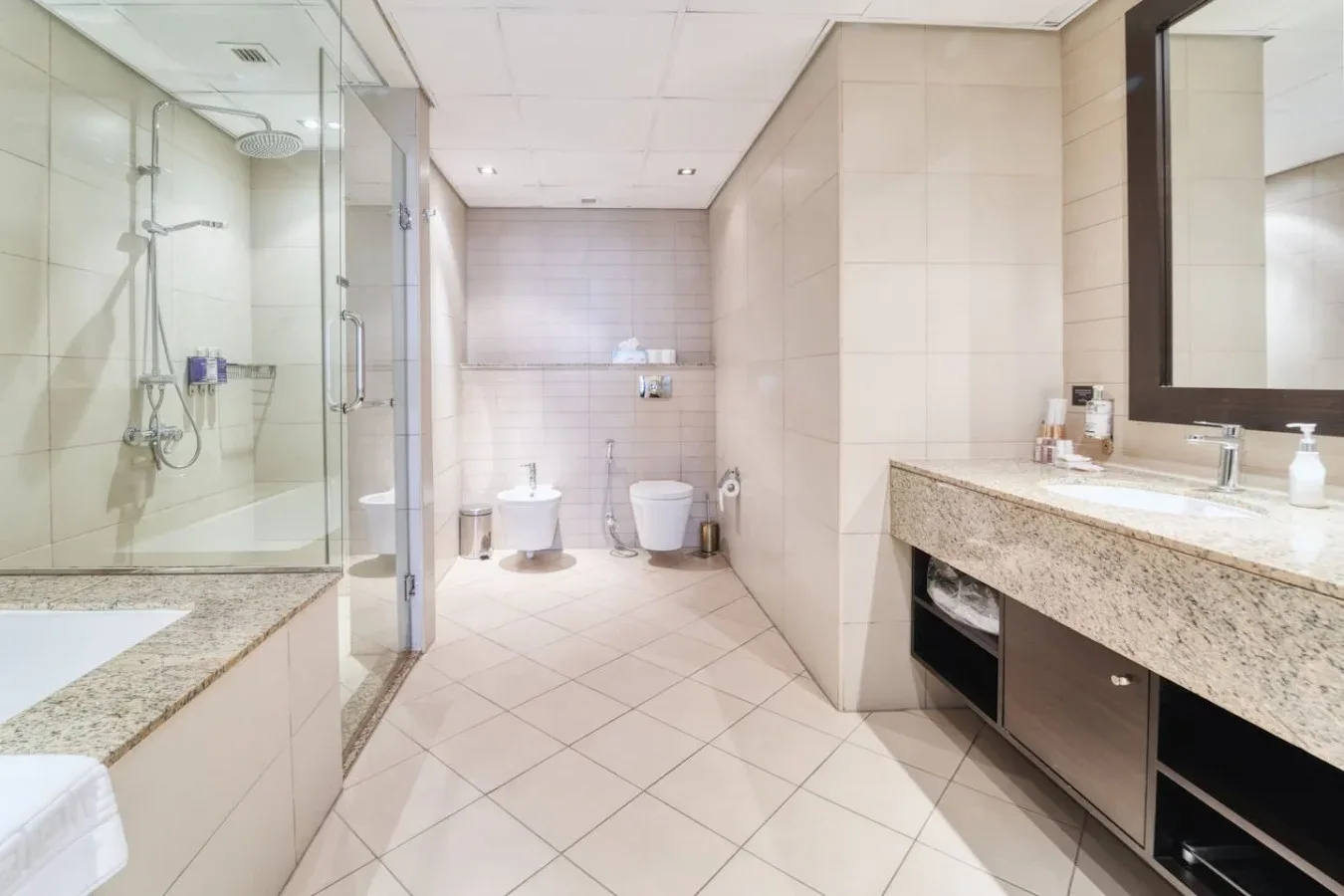 Un baño con suelo de baldosas, ducha de cristal y un lavabo alargado.
