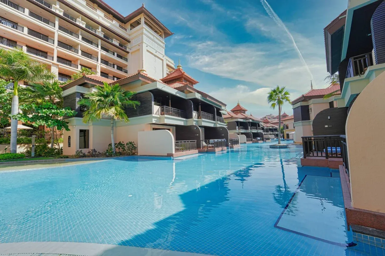 Una piscina se extiende entre edificios, con palmeras y asientos al aire libre.