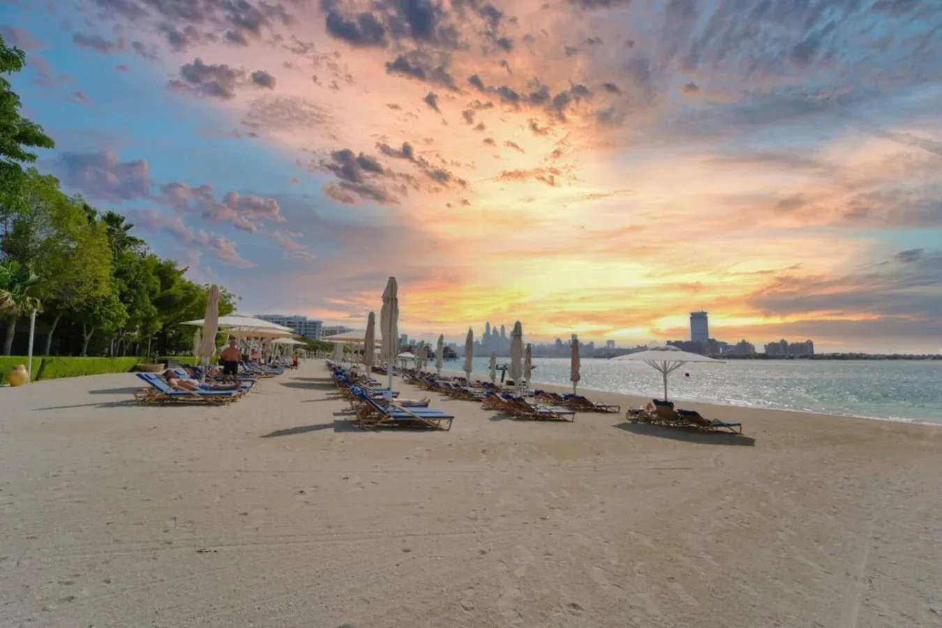 Una playa de arena con tumbonas y sombrillas bajo un cielo colorido al atardecer.