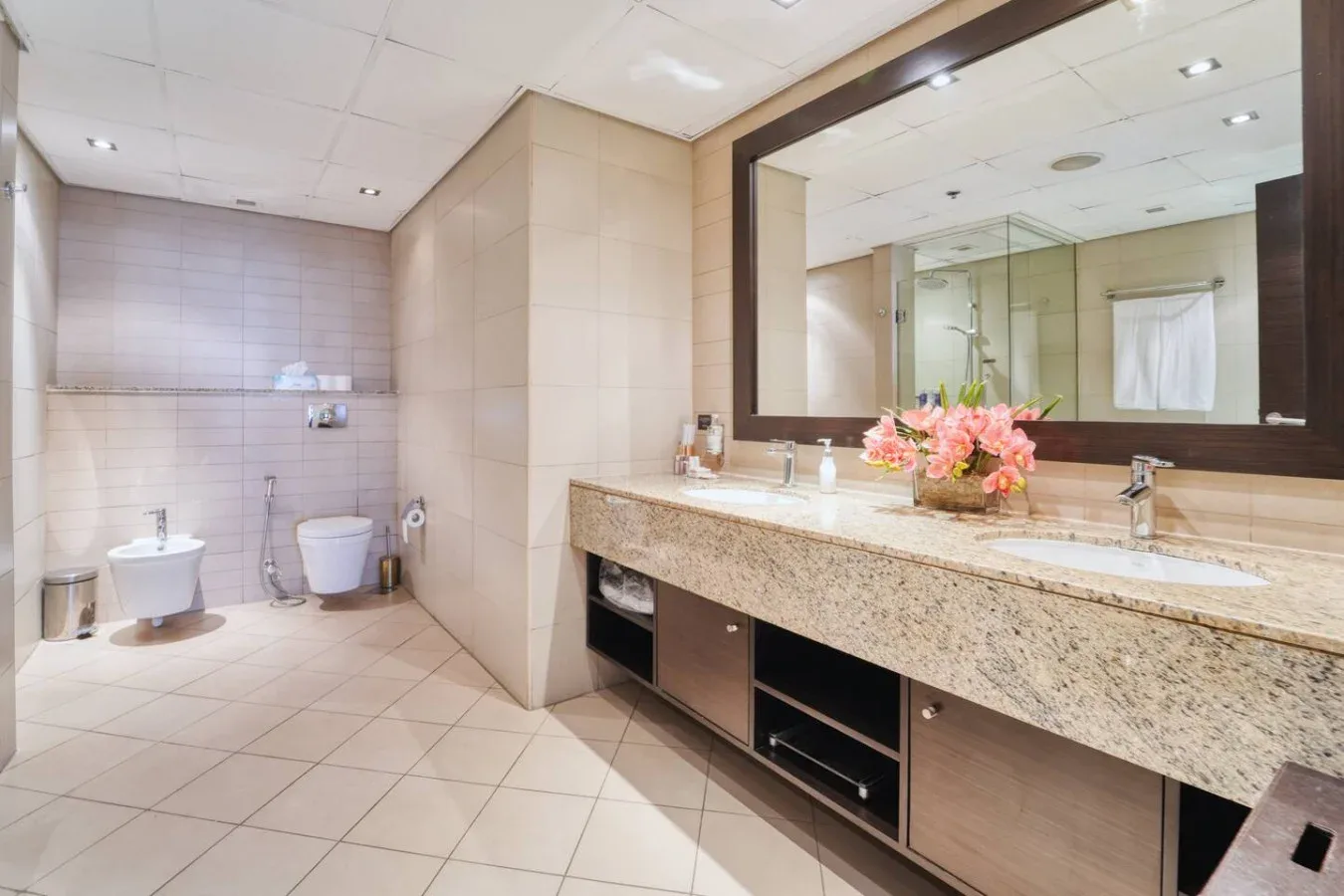 Un baño espacioso con un tocador largo, un espejo grande y flores rosas.