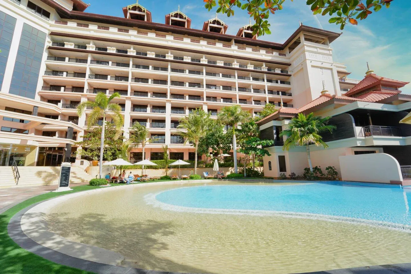 Una piscina al aire libre está frente a un edificio de varios pisos con palmeras.