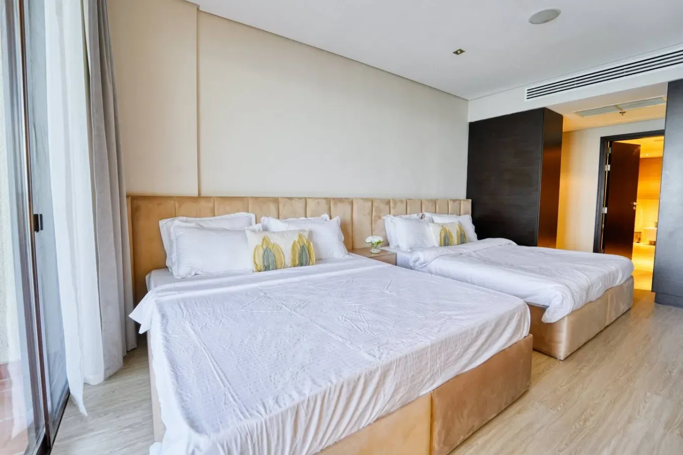 Un dormitorio luminoso con dos camas, ropa de cama blanca y cortinas largas.