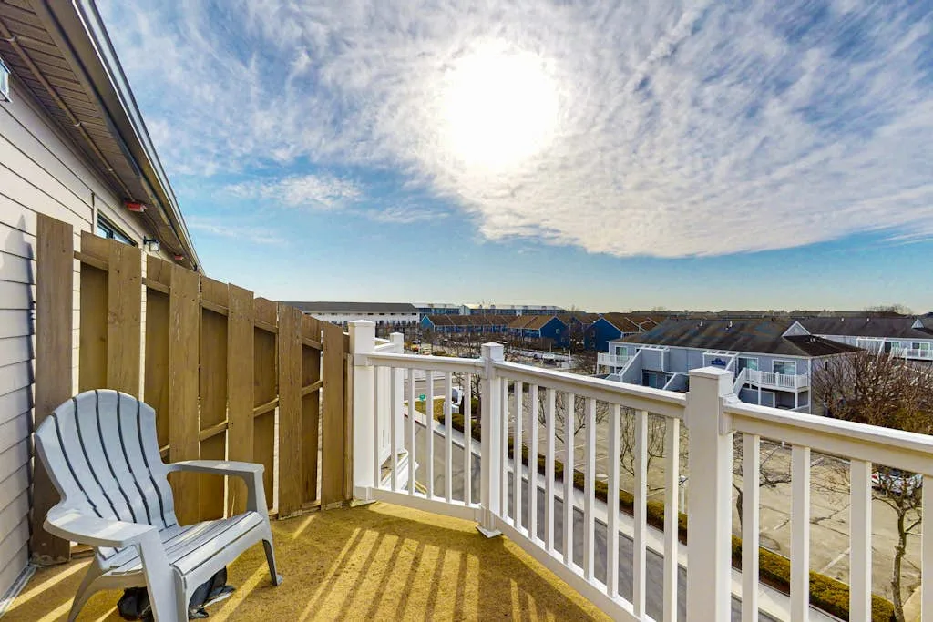 A balcony with a white railing and a chair overlooks nearby houses.