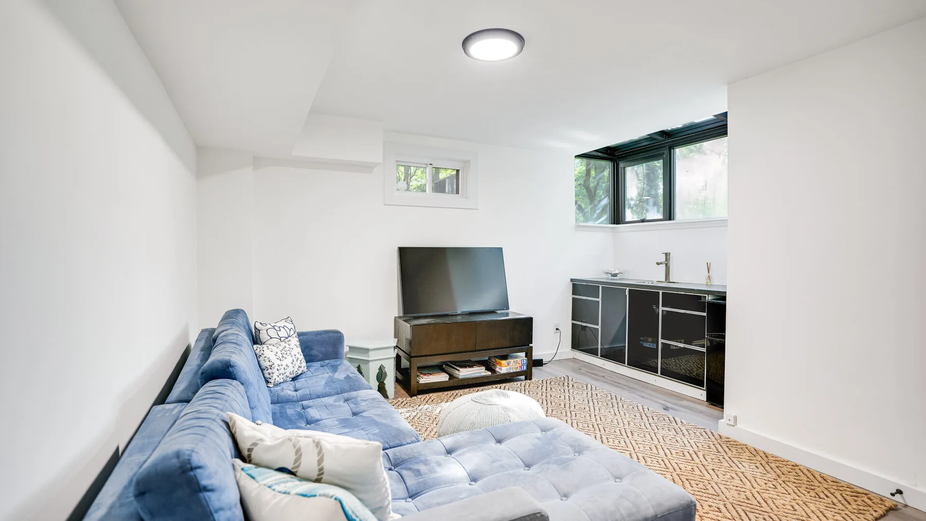Una sala luminosa con asientos azules, un televisor y una pequeña zona de cocina.