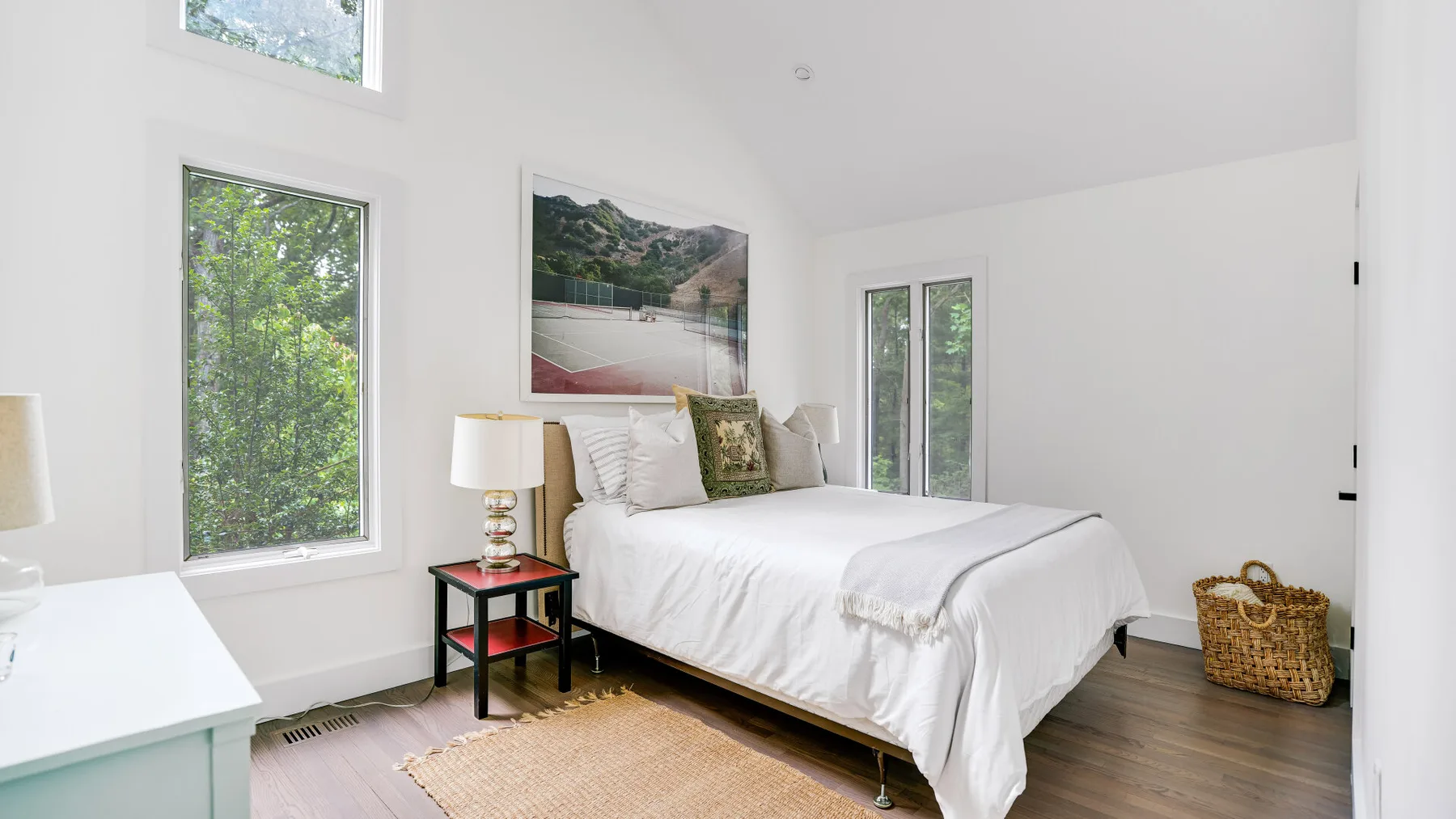 Un dormitorio luminoso con una cama blanca junto a ventanas altas.