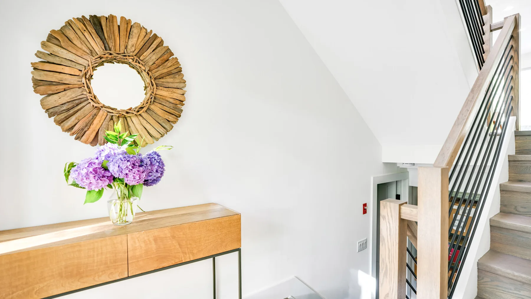 Un espacio luminoso con escaleras, una consola de madera y un espejo decorativo.