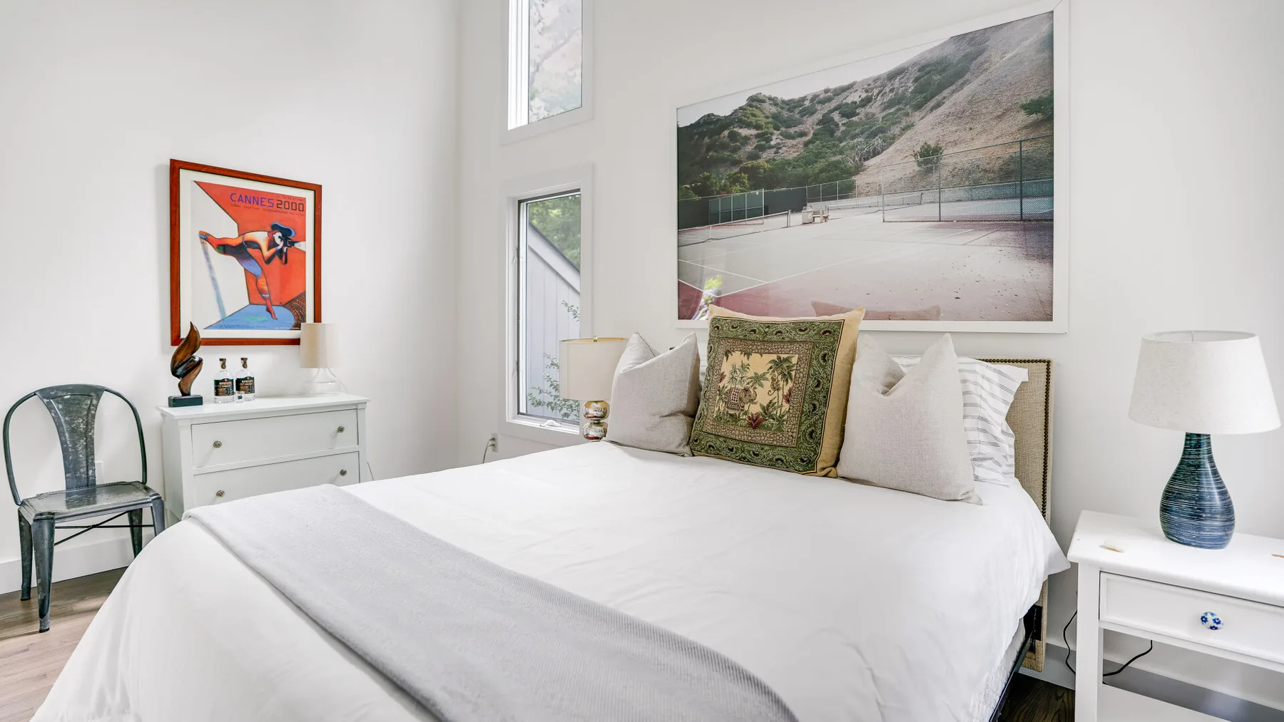 Un dormitorio luminoso con una cama bien arreglada y arte enmarcado en la pared.