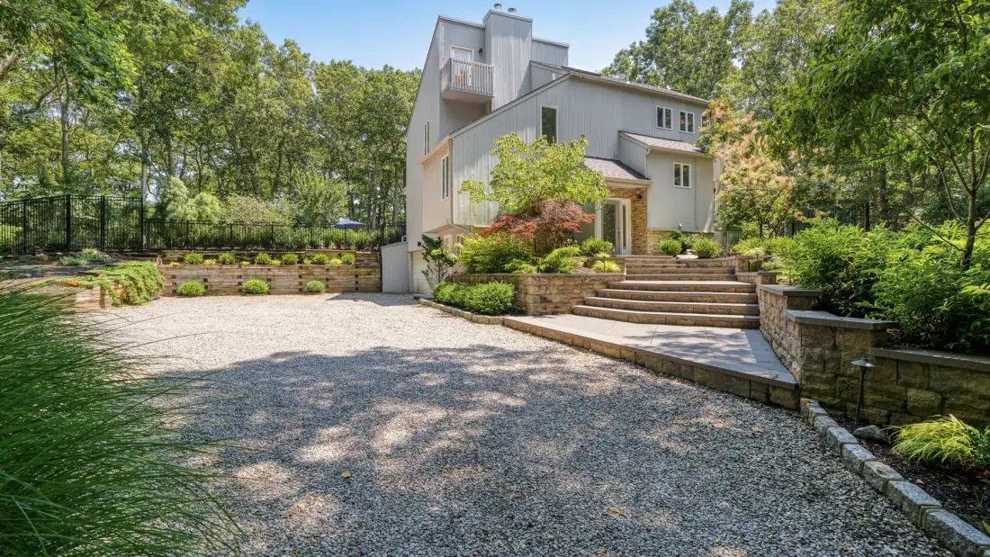 Una casa moderna se alza tras una entrada de grava, con jardines y amplios escalones.