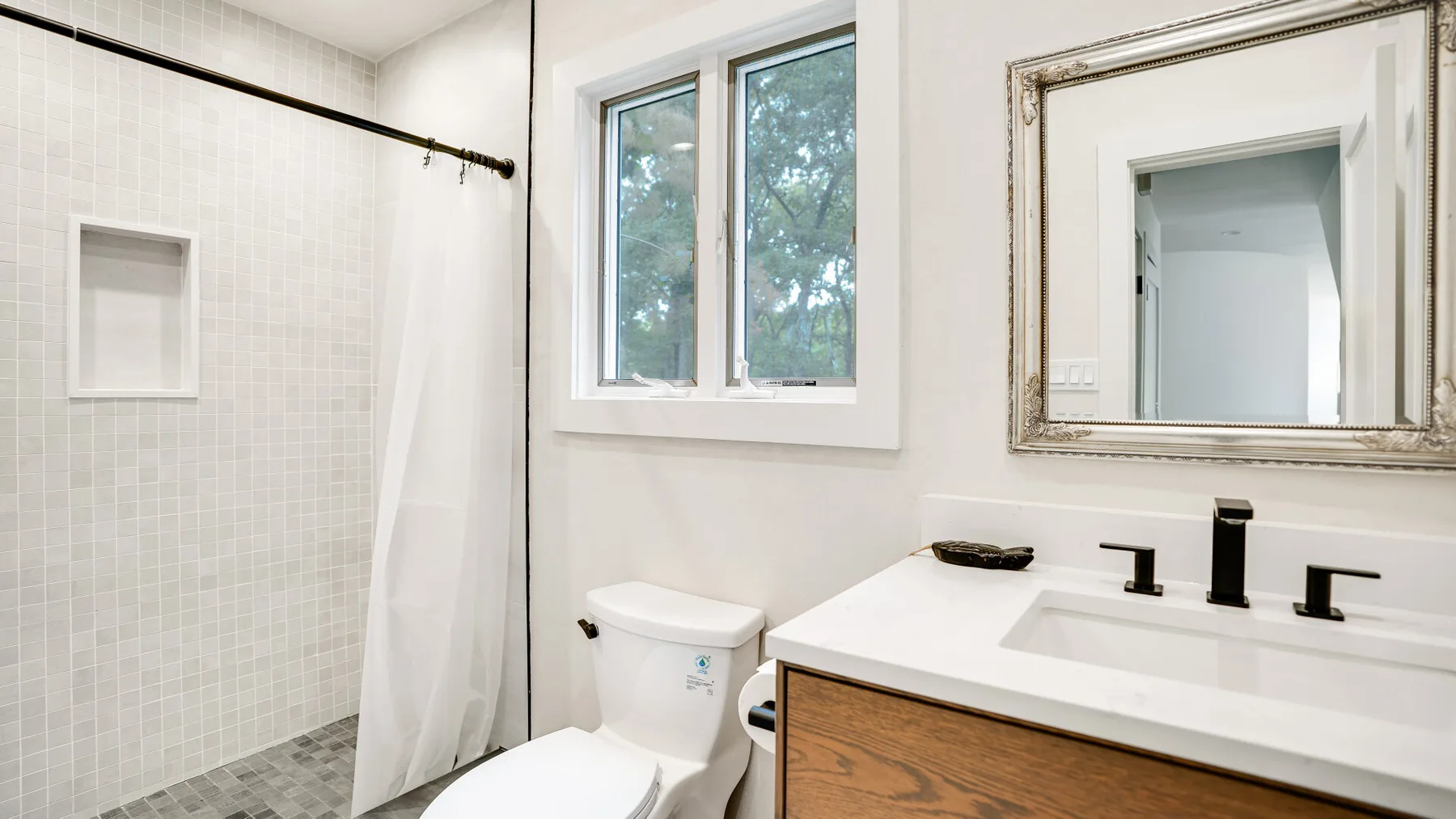 Un baño luminoso con ducha de azulejos, lavabo y ventana.