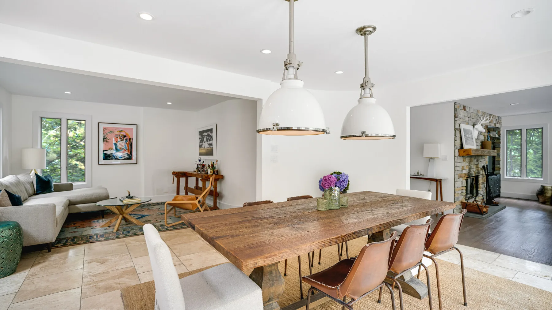 Un luminoso espacio abierto de comedor y sala de estar con una larga mesa de madera y lámparas colgantes.