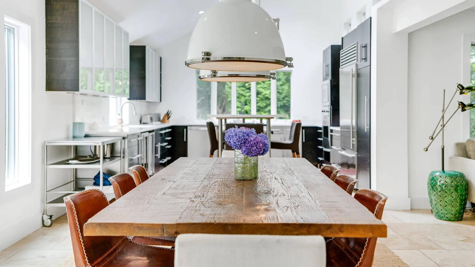Una luminosa cocina con comedor y una larga mesa de madera bajo una lámpara colgante.