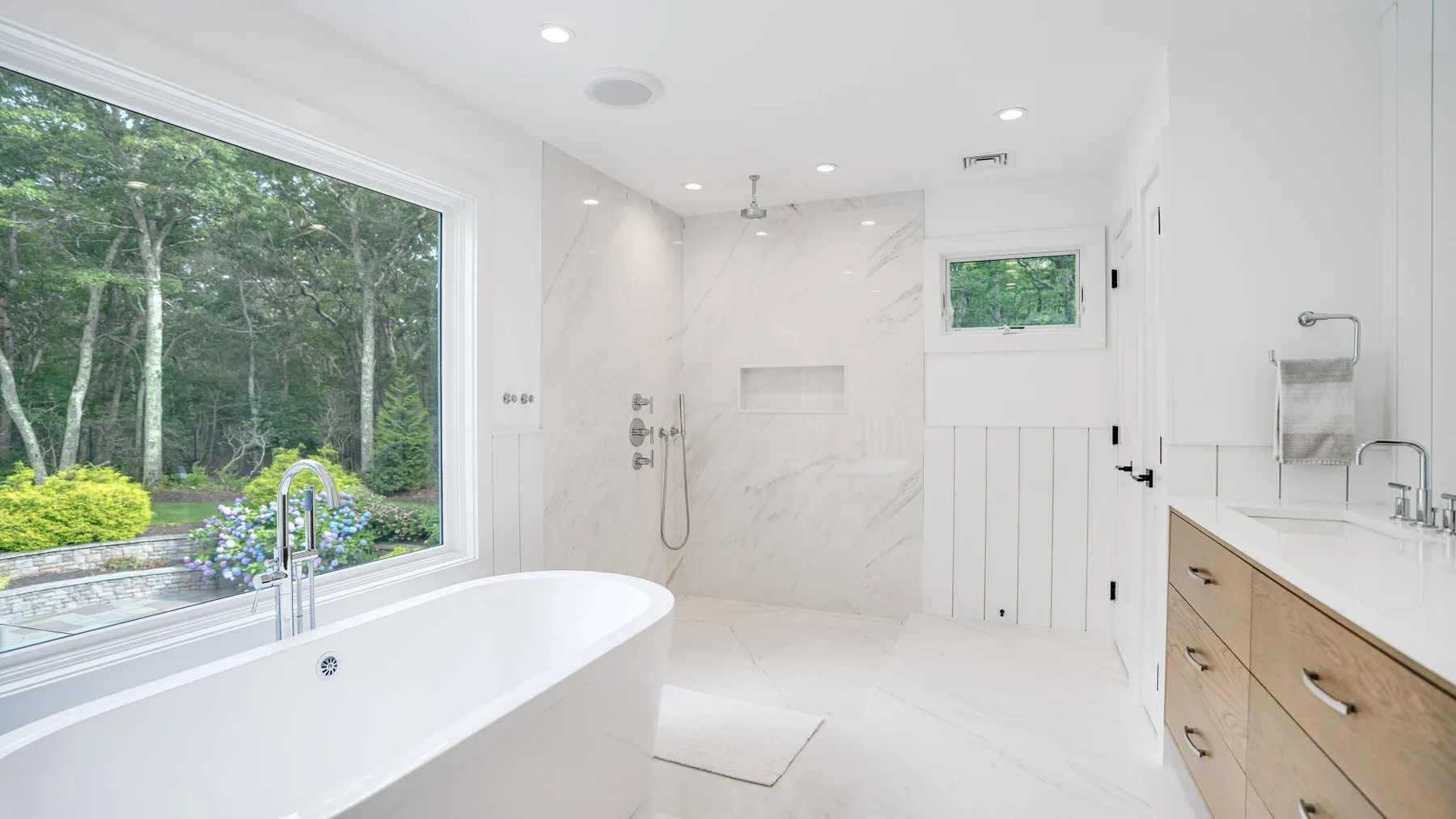 Un baño luminoso con bañera exenta, ducha y una ventana grande.