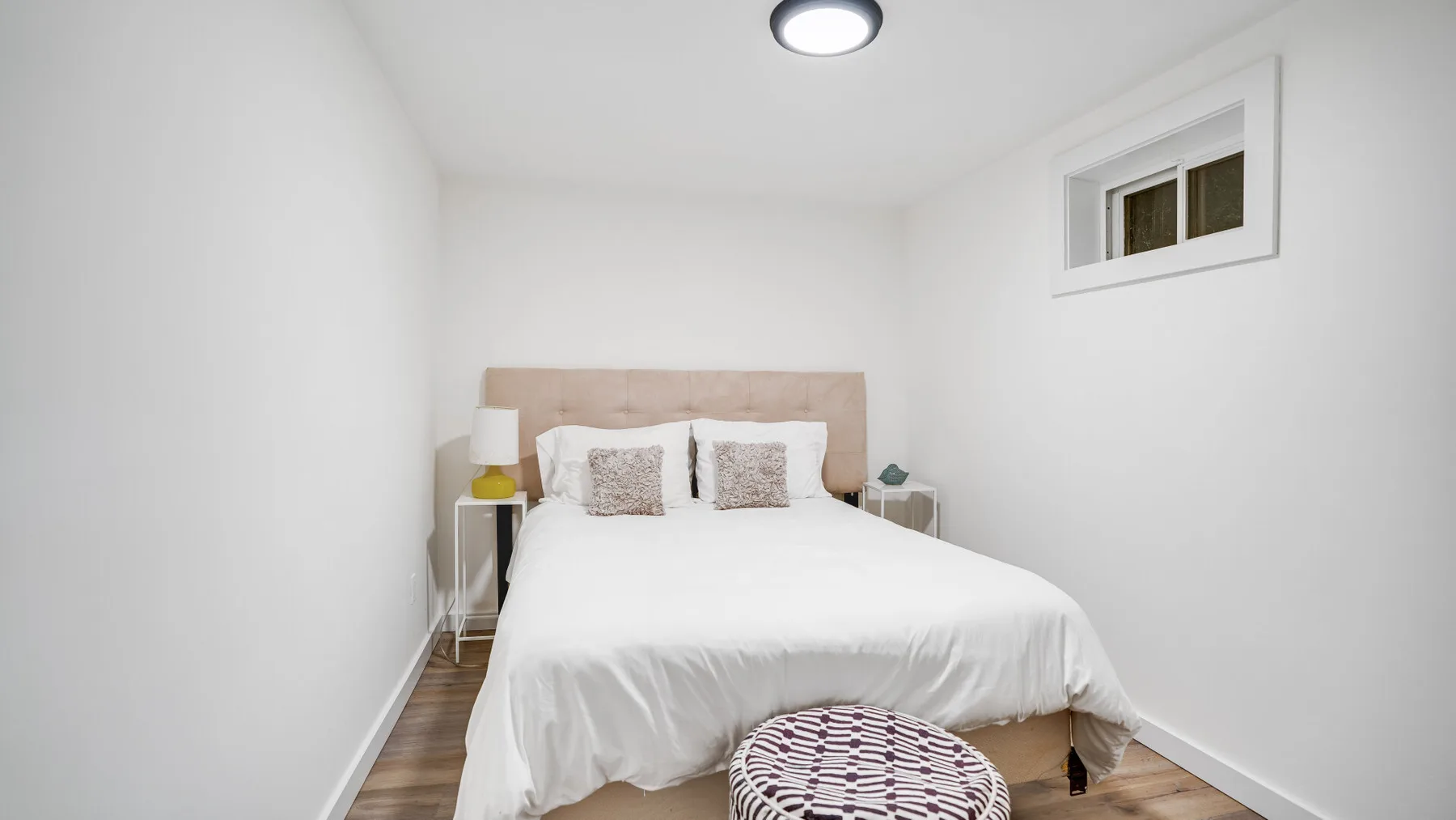 Un dormitorio luminoso con una cama bien hecha y una ventana pequeña.