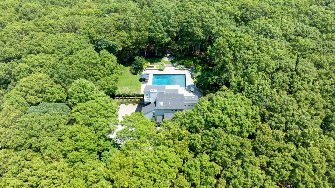 Vista aérea de una casa y una piscina rodeadas de una densa arboleda verde.
