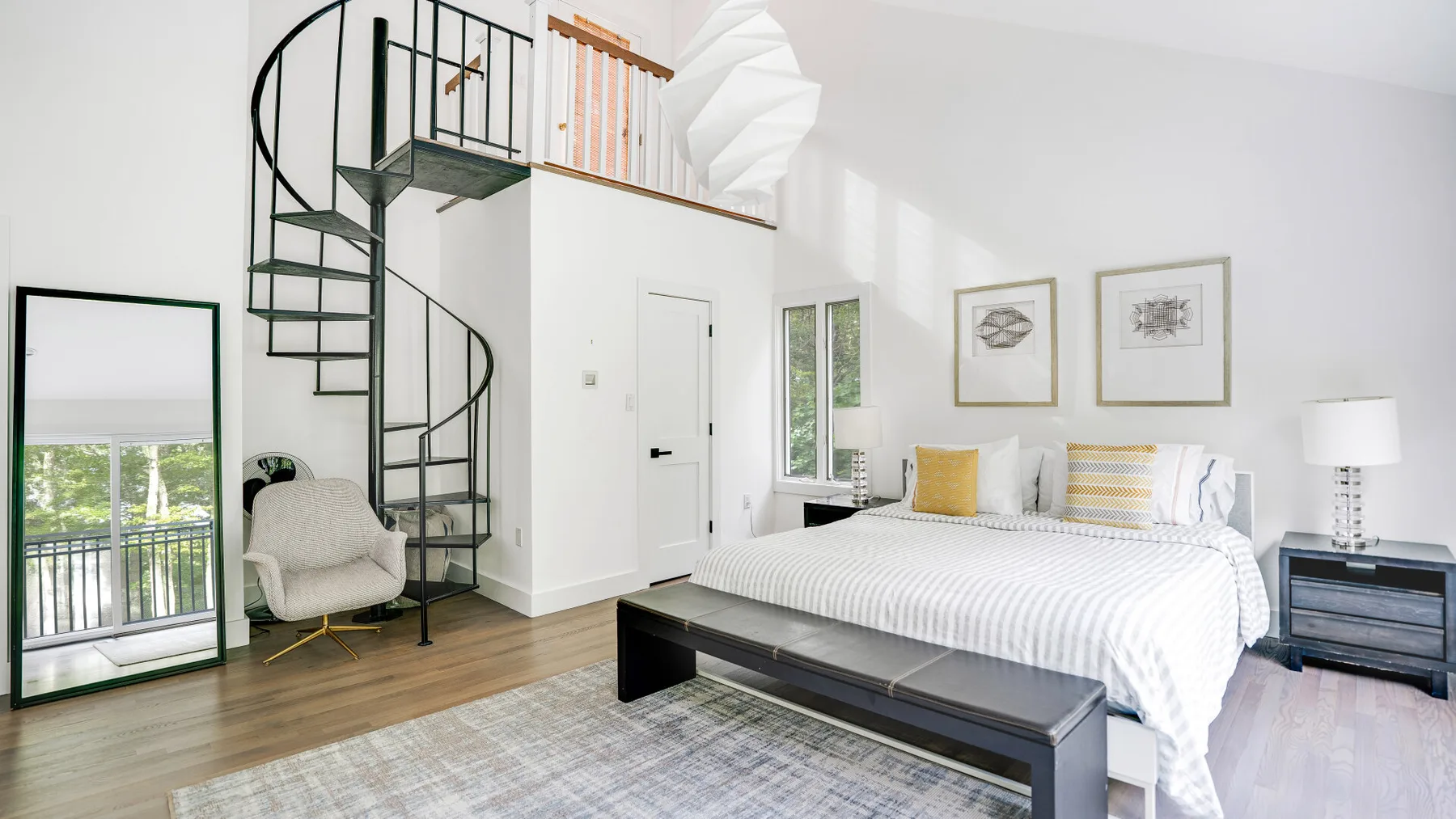 Un dormitorio luminoso con una cama, una escalera de caracol y un espejo grande.
