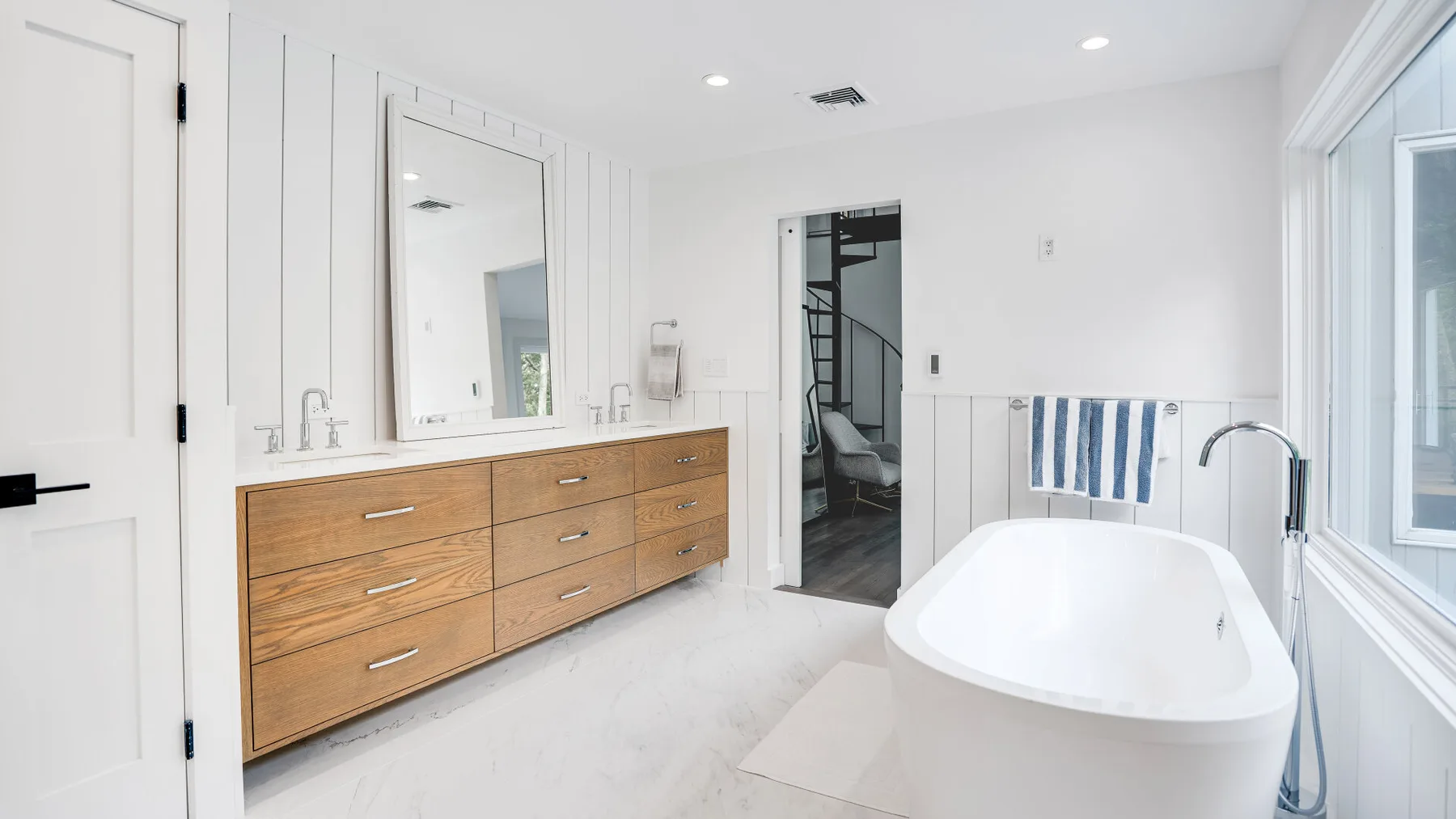 Un baño luminoso con un tocador de madera y una bañera exenta.