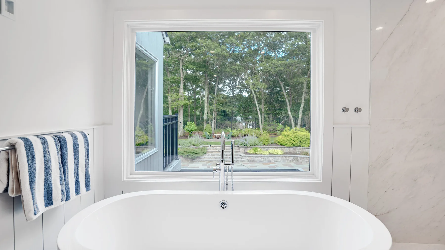Un baño con una bañera exenta bajo una ventana grande con vistas a los árboles.