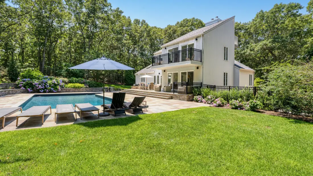 Una casa moderna se encuentra junto a una piscina, un patio y un césped verde.