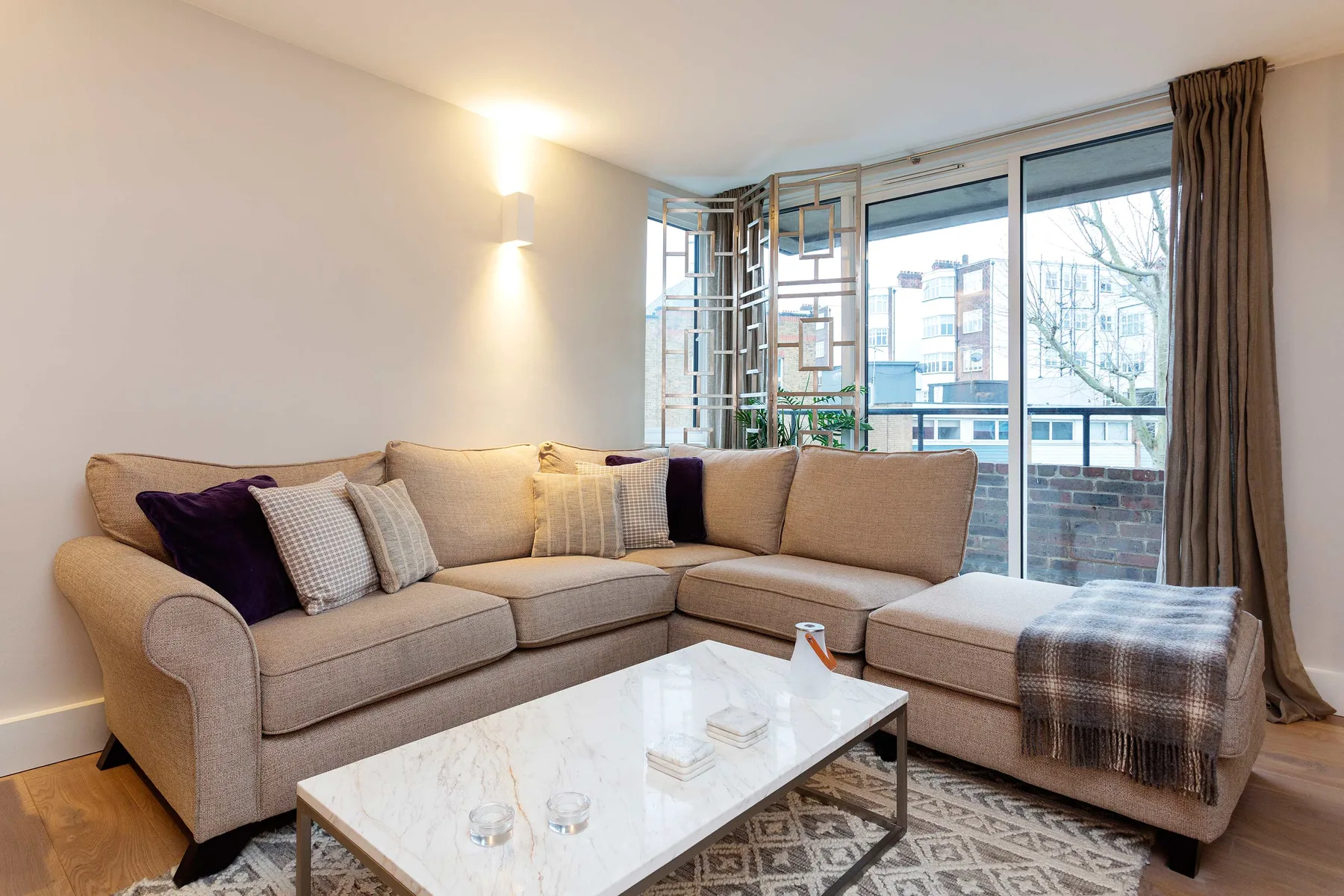 A bright living room with a beige sectional and a large window.
