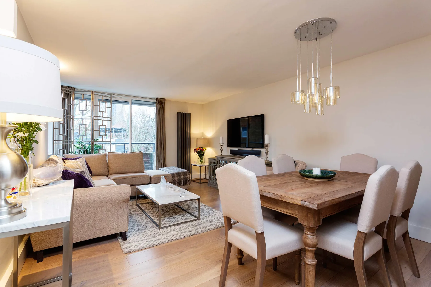 A living and dining area with a sofa, a wooden dining table, and large windows.