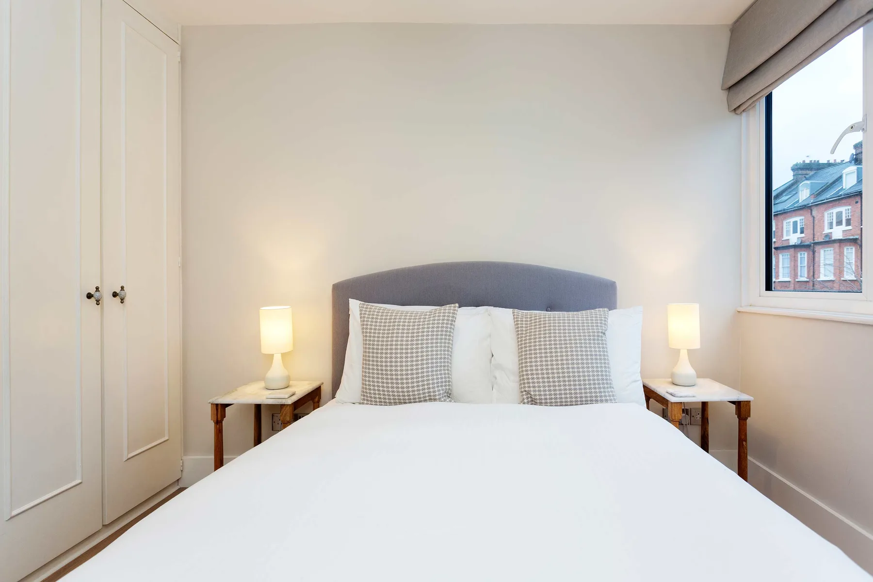 A bright bedroom with a neatly made bed and matching bedside lamps.