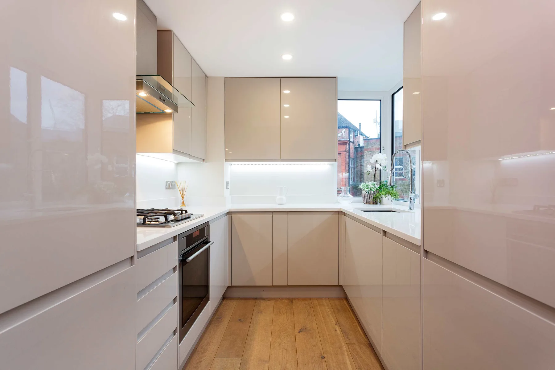 A modern kitchen with pale cabinetry, a cooktop, and a window overlooking greenery.