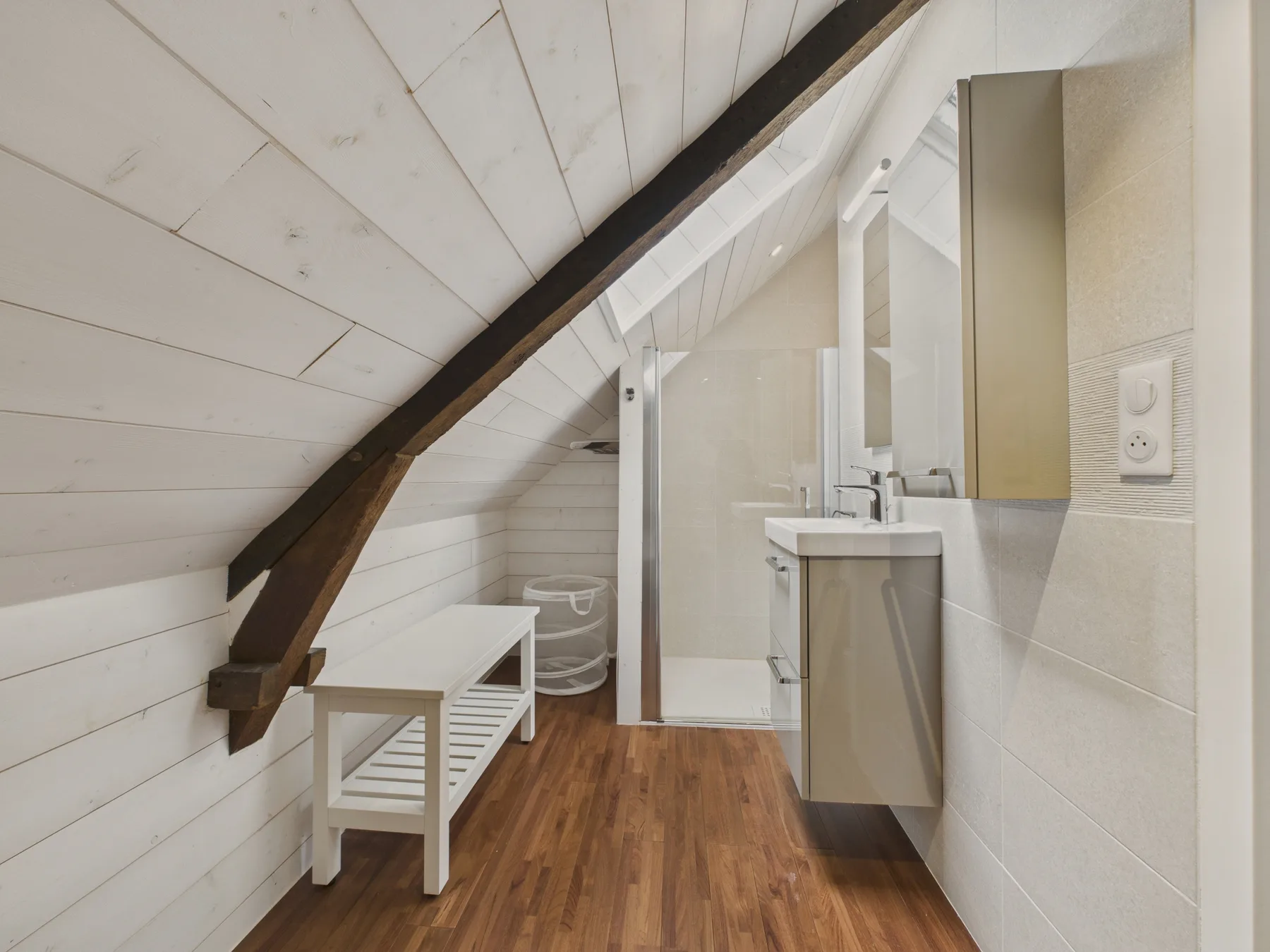 A bathroom beneath a sloped ceiling, with a sink and shower.