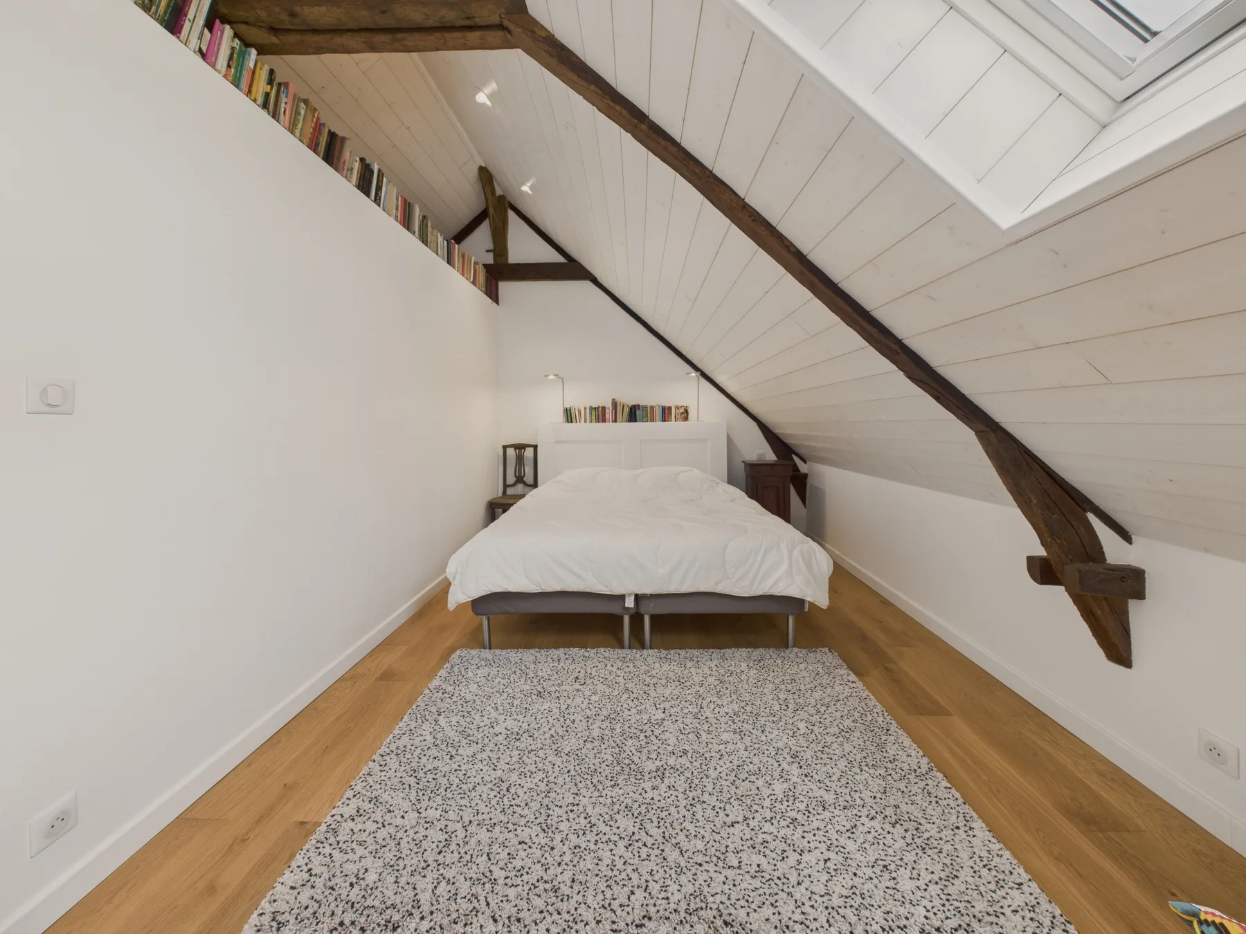 An attic bedroom with a bed beneath a sloped ceiling and exposed beams.