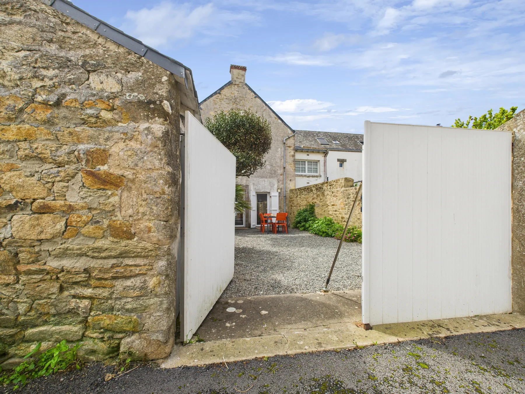 A stone house courtyard entrance with open white gates and outdoor seating.