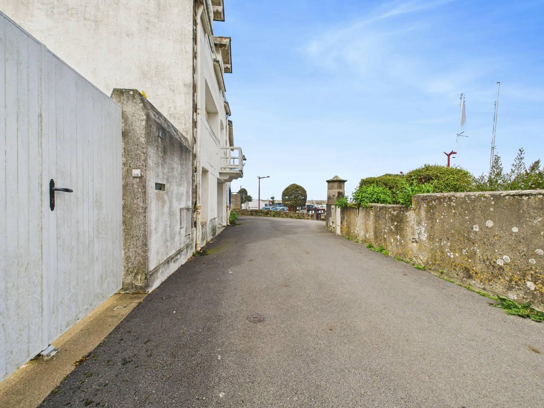A paved lane runs between a white building and a low stone wall.