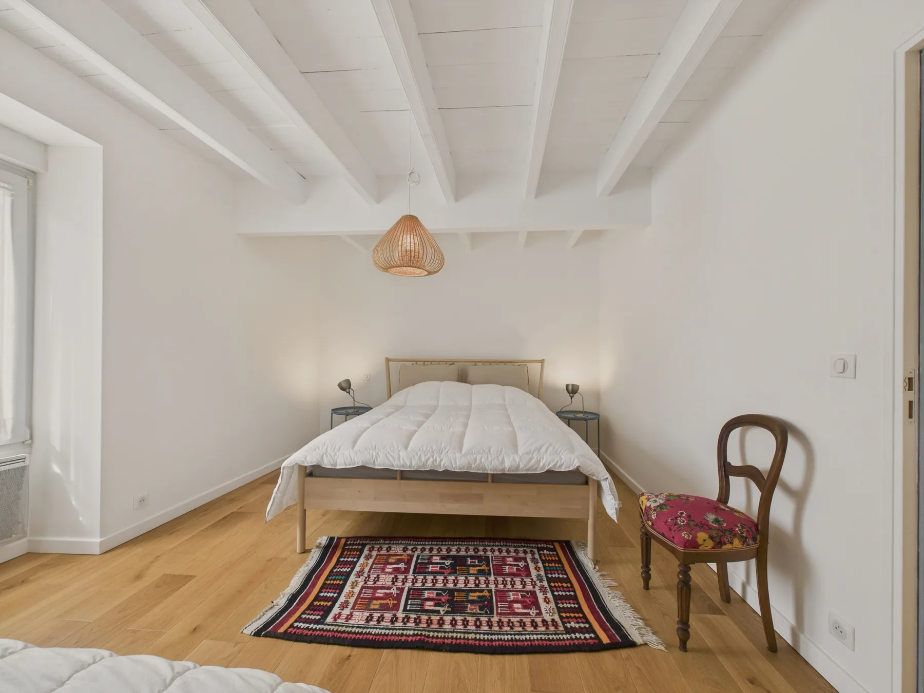 Bedroom with a wooden bed, patterned rug, and exposed ceiling beams.
