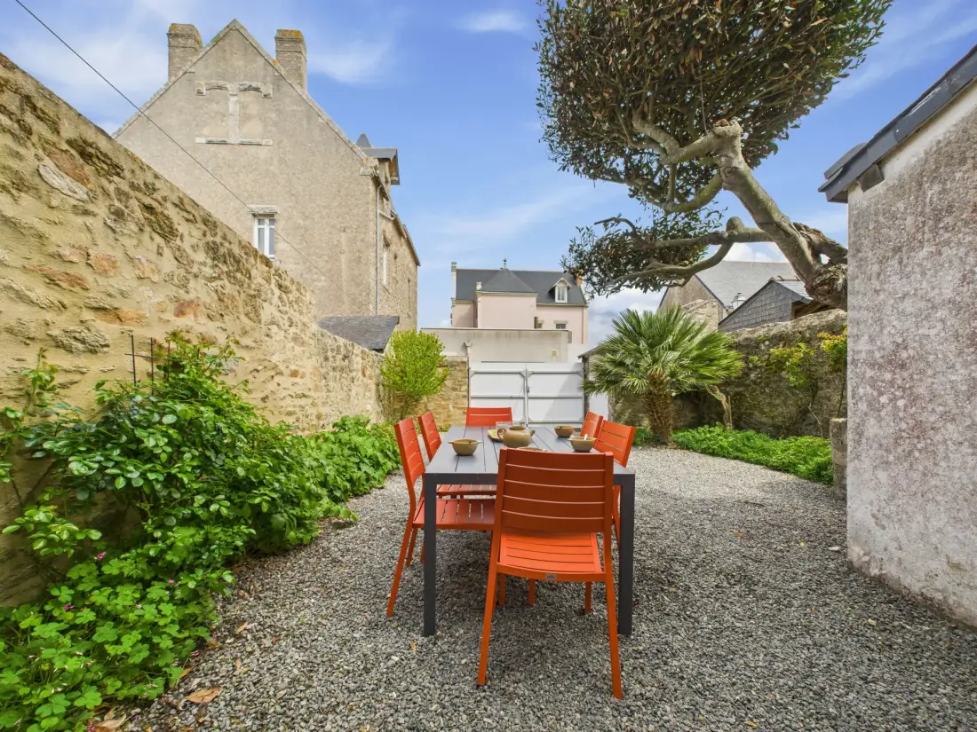 A gravel courtyard with an outdoor dining table and chairs among stone walls and greenery.