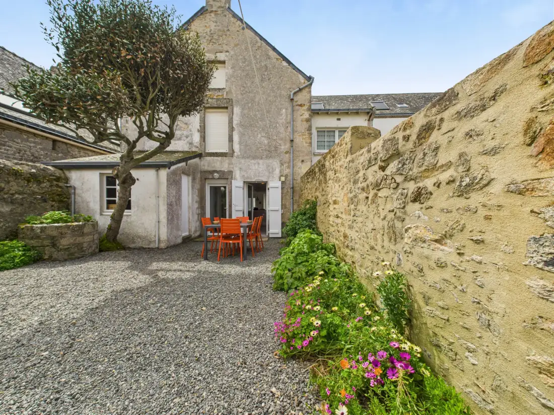 A gravel courtyard with outdoor seating, flowering plants, and stone walls.