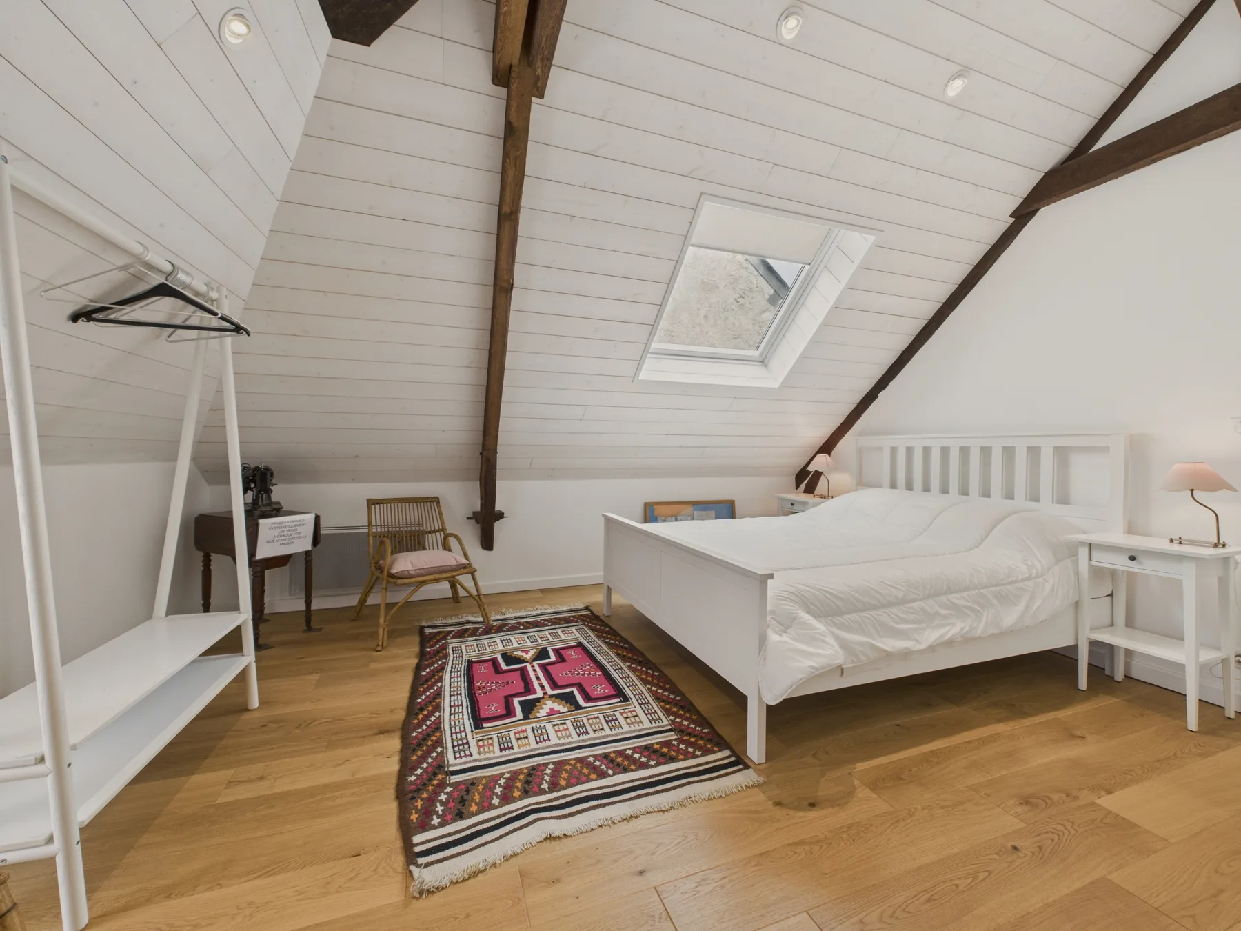 A bright attic bedroom with a bed, skylight, and patterned rug.