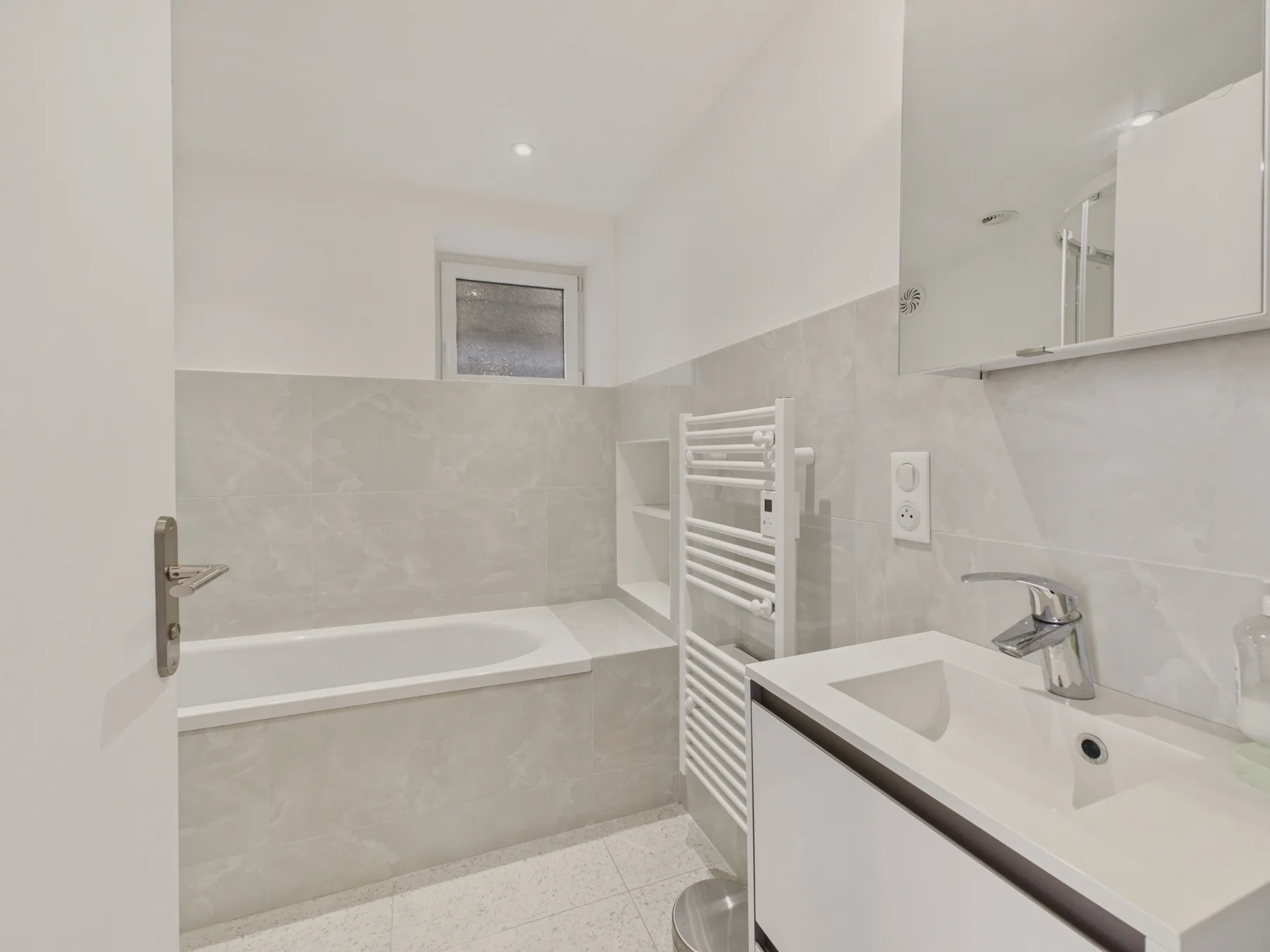 A bright bathroom with a bathtub, sink, and wall-mounted towel rail.