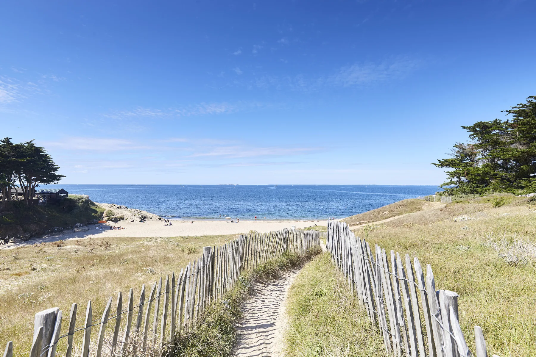 A sandy path runs between wooden fences toward the beach and sea.