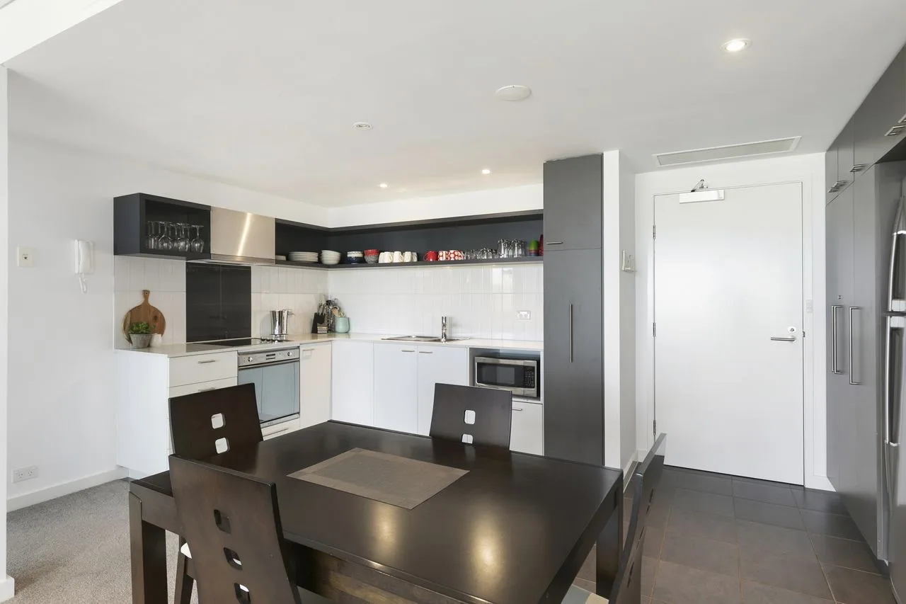 A modern kitchen and dining area with a dark table and white cabinetry.