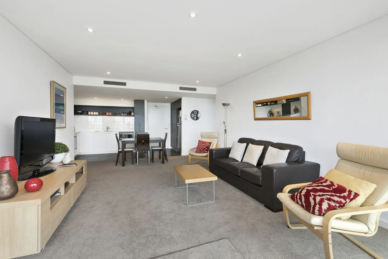 A living room with a seating area and an open kitchen in the background.