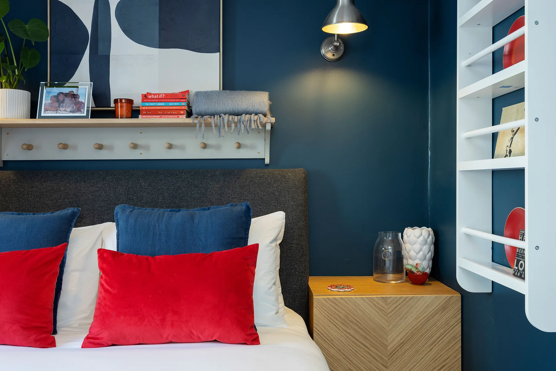 A bedroom with a bed dressed in white linens and red and blue pillows.