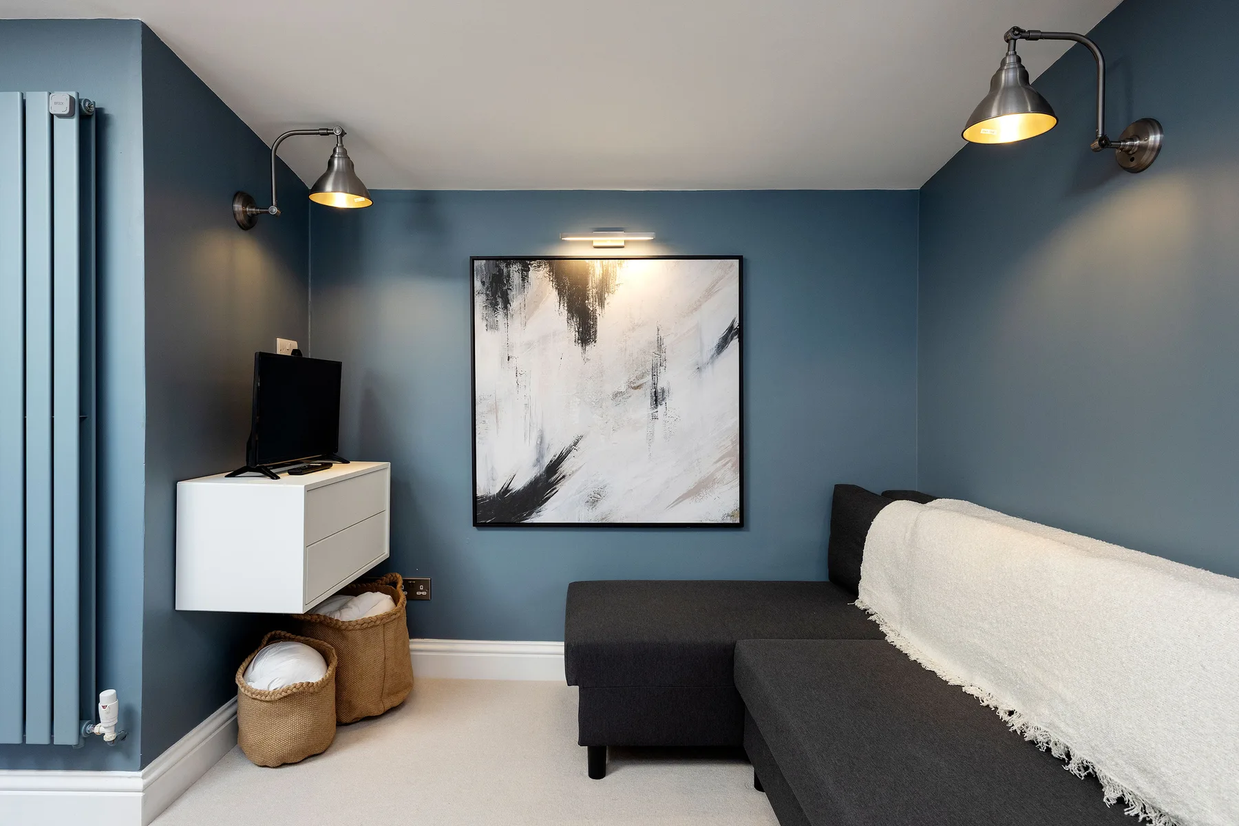 A blue-walled living room with dark seating and an abstract painting.