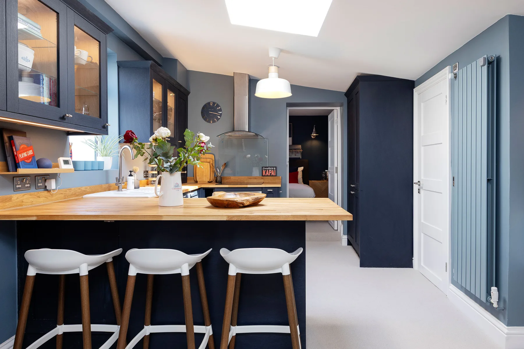 A modern kitchen with a long counter, bar seating, and dark blue cabinetry.