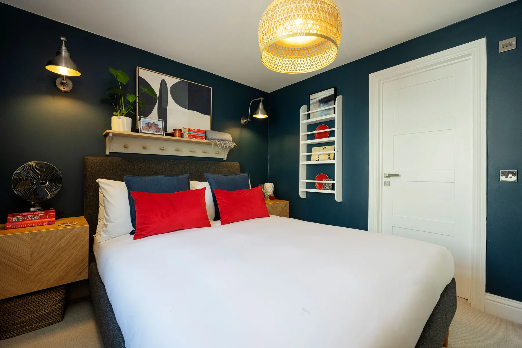 A bedroom with a neatly made bed, dark walls, and a white door.