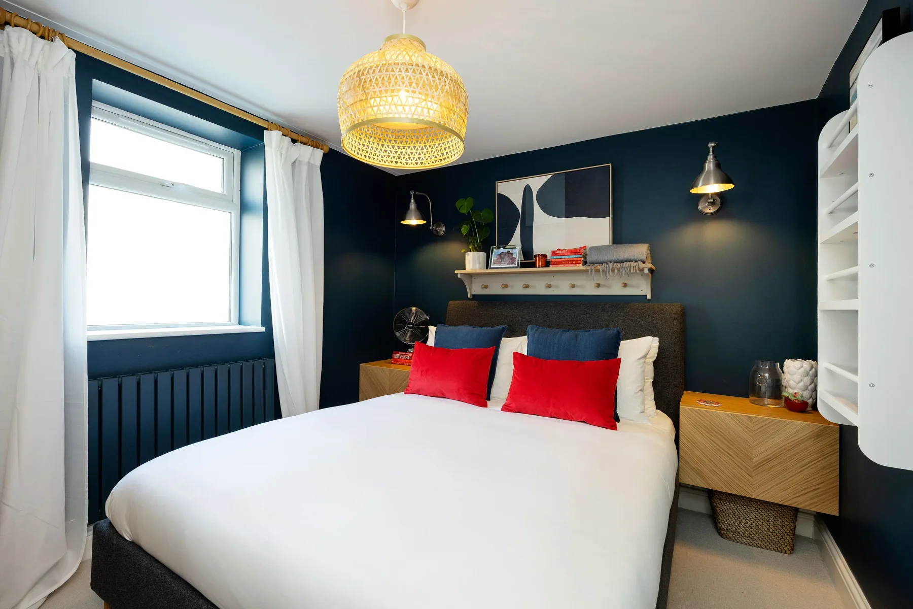 A bedroom with a bed, red accent pillows, and dark blue walls.