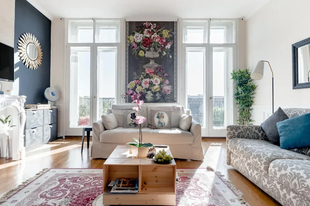 A bright living room with sofas, tall windows, and floral wall art.